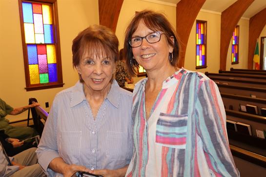 Two women smile together in a cheerful atmosphere during a community event inside a church.