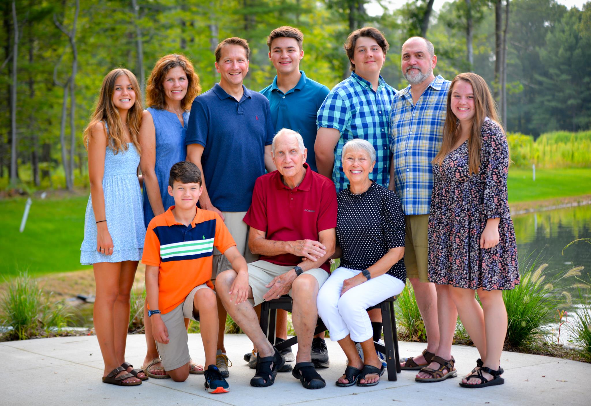 A joyful family poses together outdoors, showcasing smiles and summer outfits by the water.