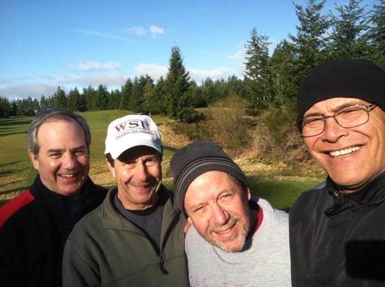 Four friends share a joyful moment outdoors on a golf course under a clear blue sky.