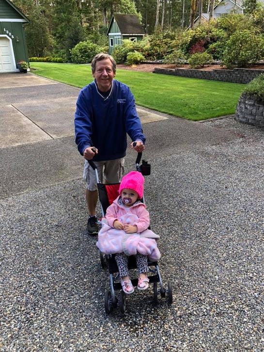 A cheerful grandfather strolls along a gravel path with his granddaughter in a stroller.