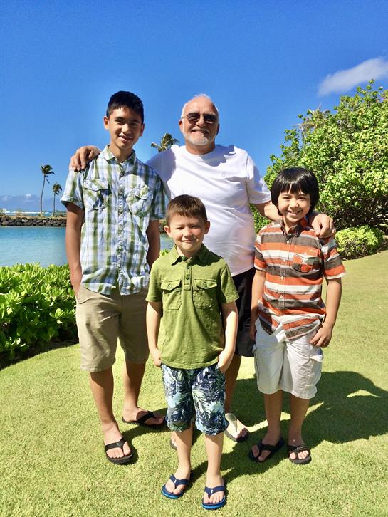 A grandfather poses happily with his four grandsons in a lush outdoor setting.