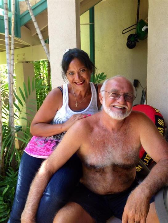 A smiling man and woman pose happily, surrounded by lush greenery under warm sunlight.