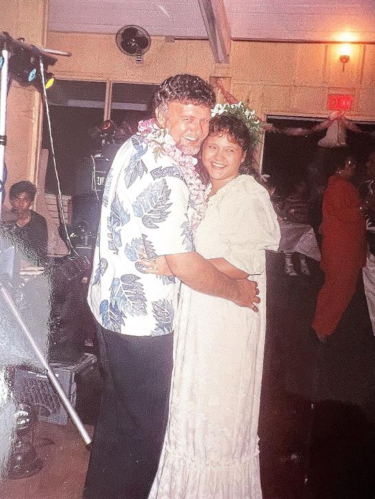 A couple dances closely at a festive gathering, surrounded by friends and lively decorations.