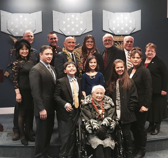 Family members gather indoors, smiling in formal attire during a celebration.