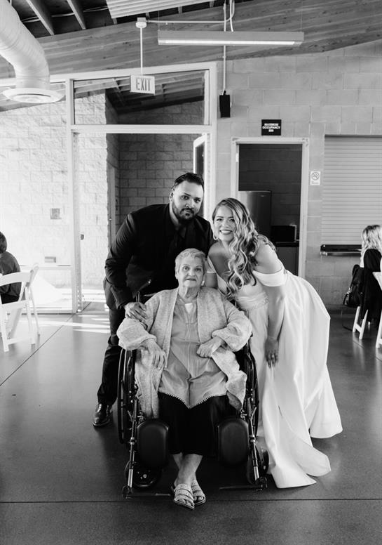 Bride and groom pose happily with grandmother, celebrating a special day in a bright venue.
