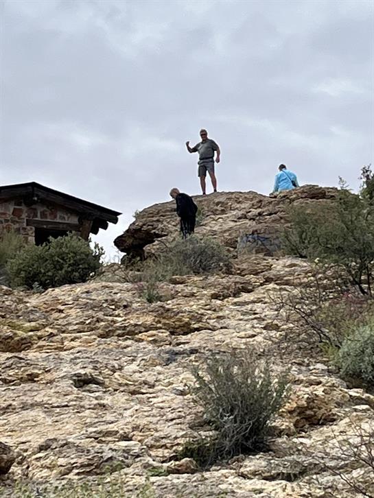 A group of individuals explore a rocky hilltop while cloudy skies loom overhead.