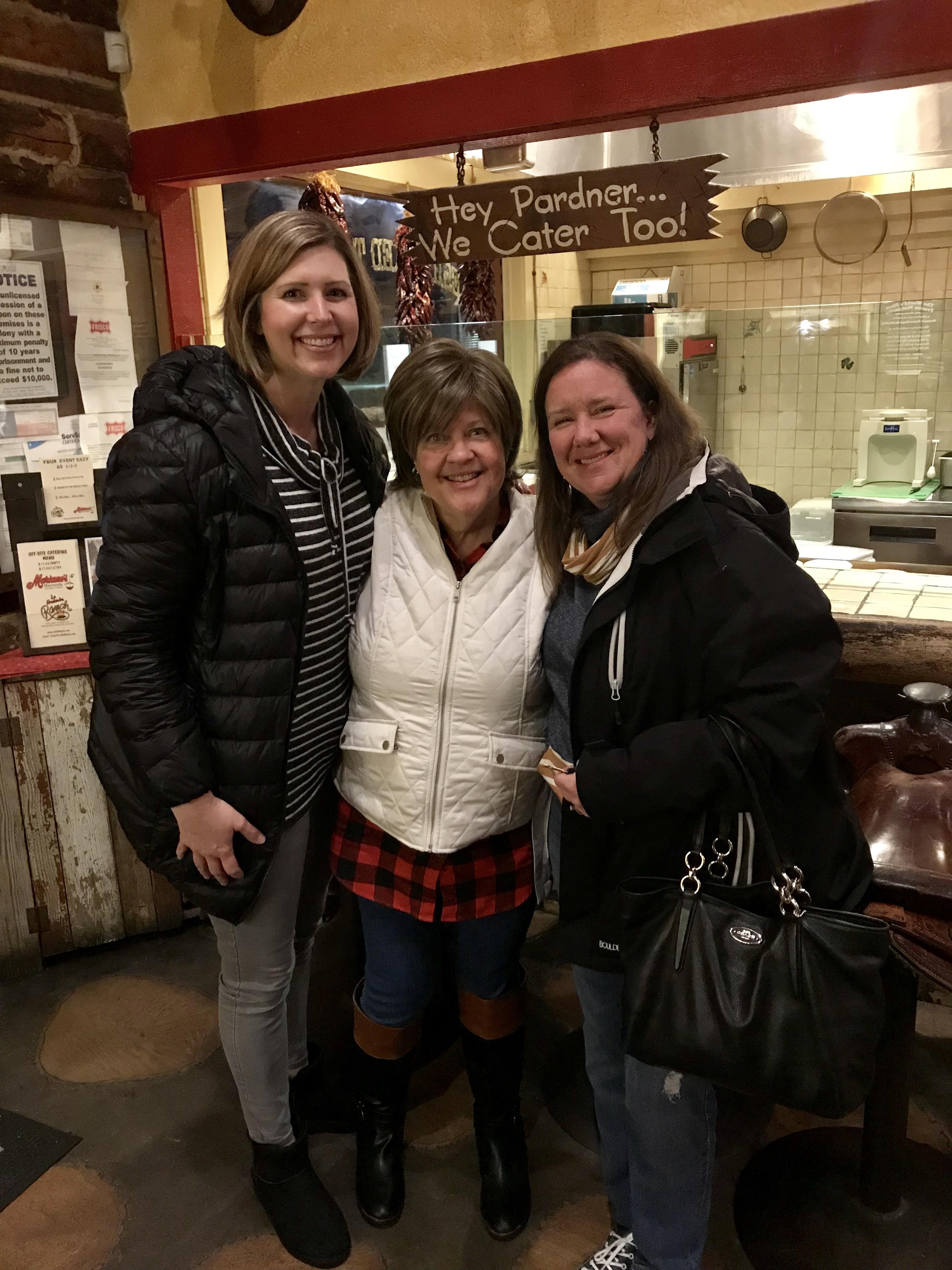 Three friends pose together in a warm restaurant, smiling and enjoying their evening.