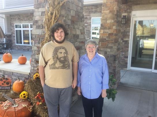 Two individuals stand in front of a building adorned with pumpkins and autumn decorations.