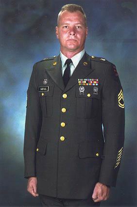 A soldier stands upright in a military uniform with medals shown on the chest in a studio.