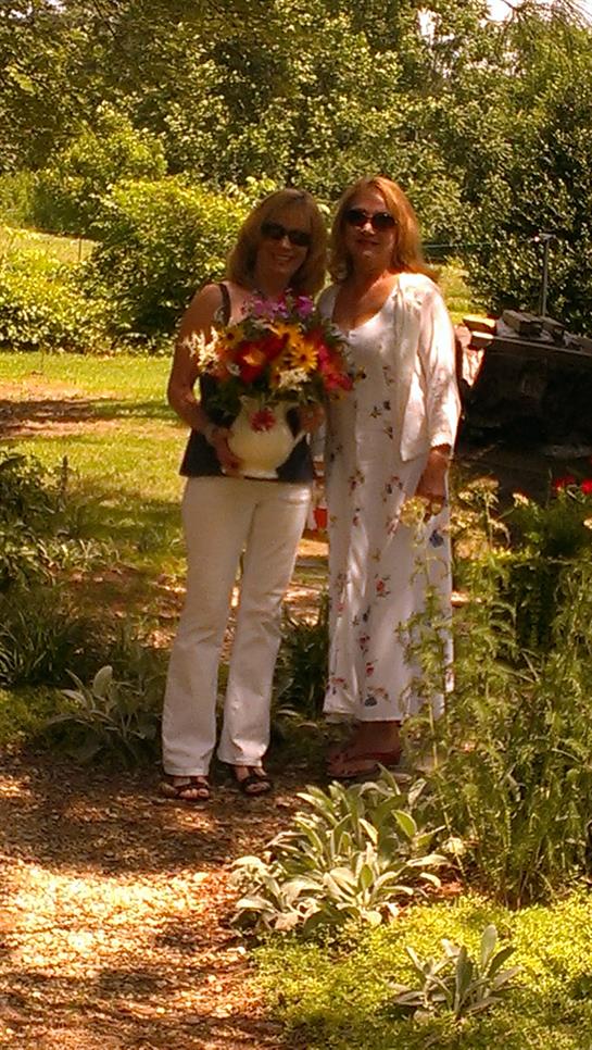 Women smile and showcase a colorful bouquet in a vibrant garden setting.
