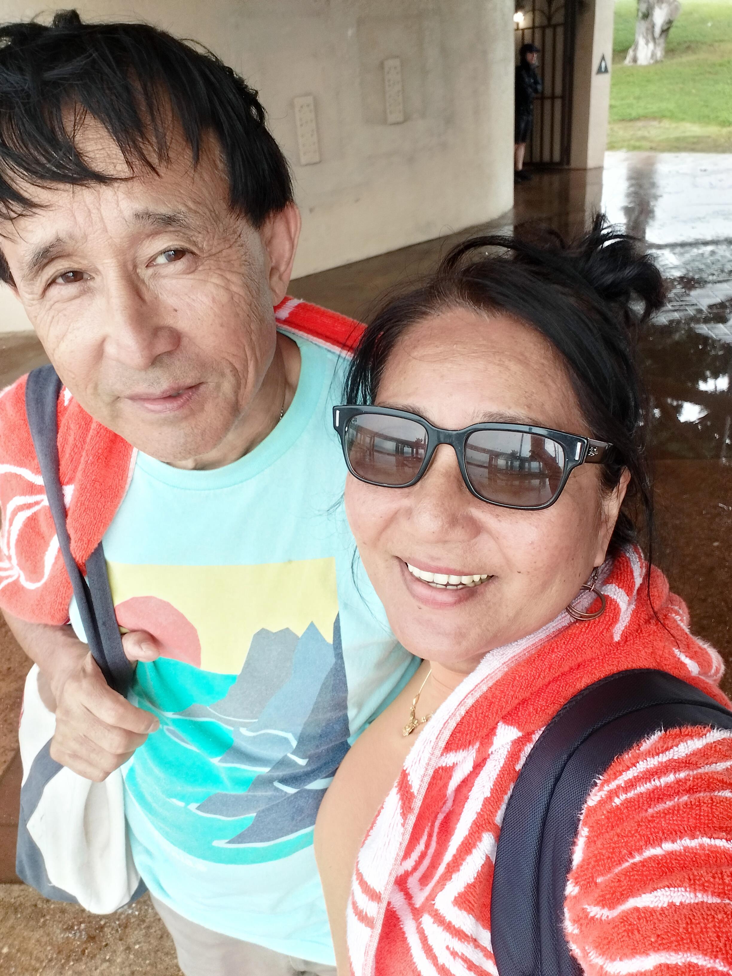Two smiling individuals embrace the warmth of the sun, wrapped in colorful towels after swimming.