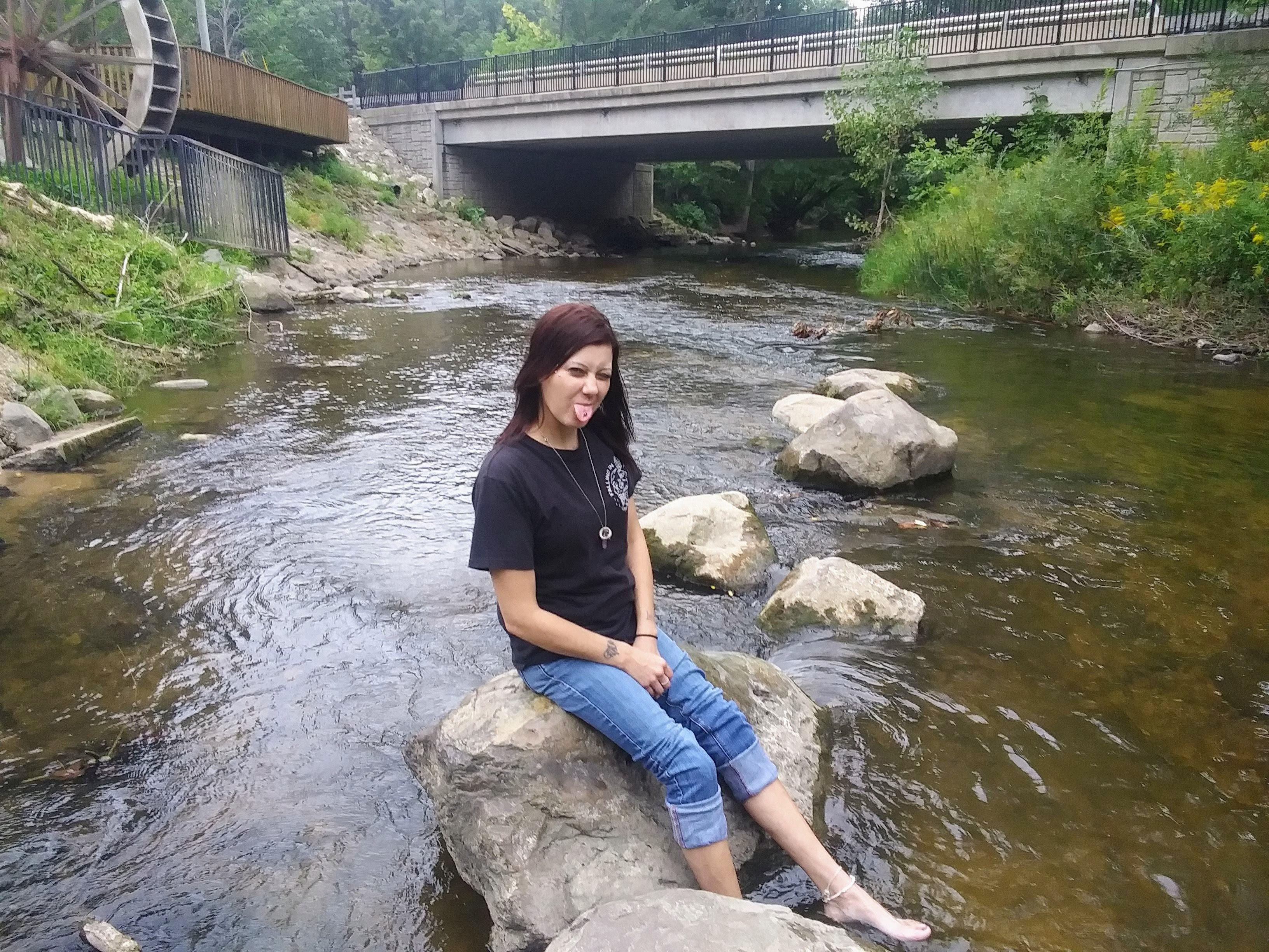 A young woman enjoys a peaceful moment while sitting on a rock in the stream.