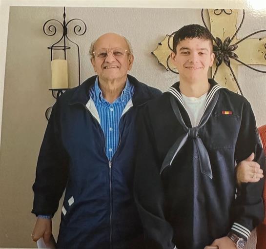 Joyful grandfather and grandson stand together after the grandson's naval graduation ceremony.