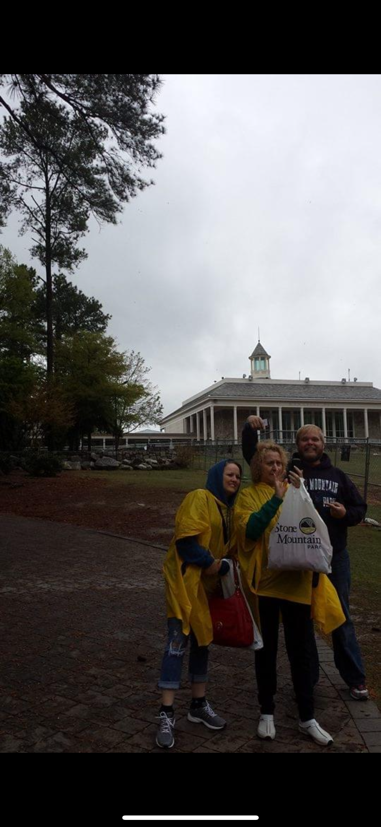 Friends laughing together in yellow ponchos during a rainy outing near a historic structure.