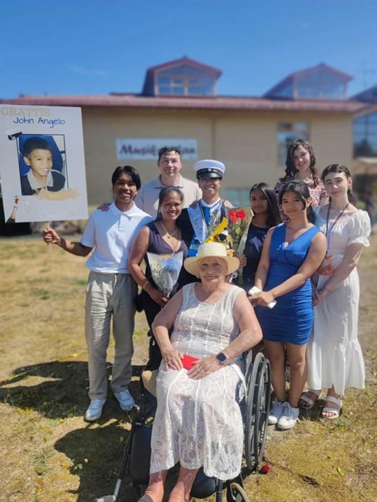 A cheerful gathering shows family and friends celebrating John Angelo with posters and smiles.