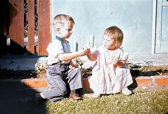 Young boy and girl share ice cream cones, playing together in a sunny backyard setting.