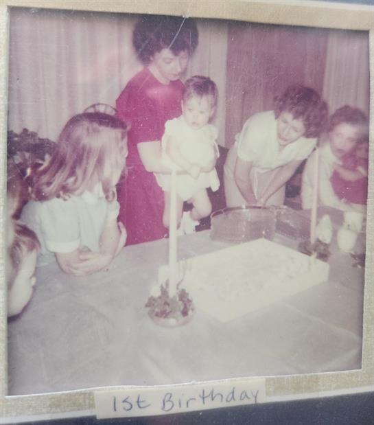 Family members gather around a table to celebrate a child's first birthday with cake and joy.
