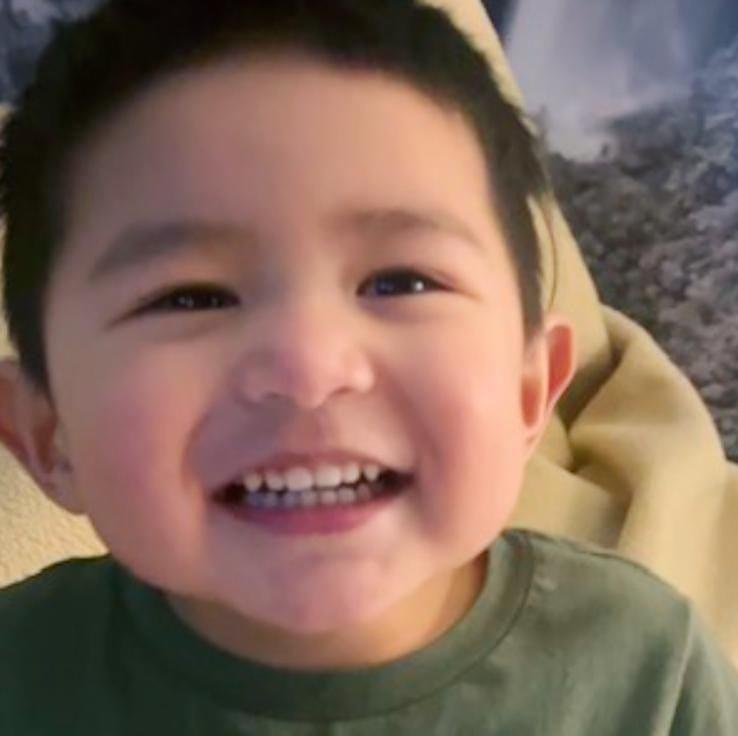 A boy with a big smile is playing on a soft blanket at home, enjoying a moment of happiness.