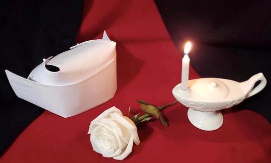 A white porcelain lamp with a lit candle and a rose adorn a rich red and black backdrop.