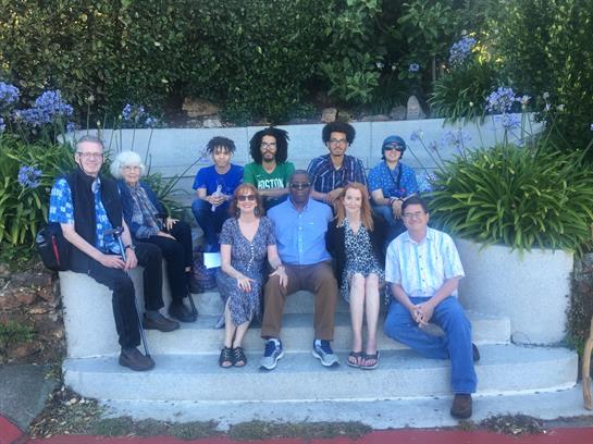 Ten people sit on garden steps, enjoying each other's company on a sunny day.