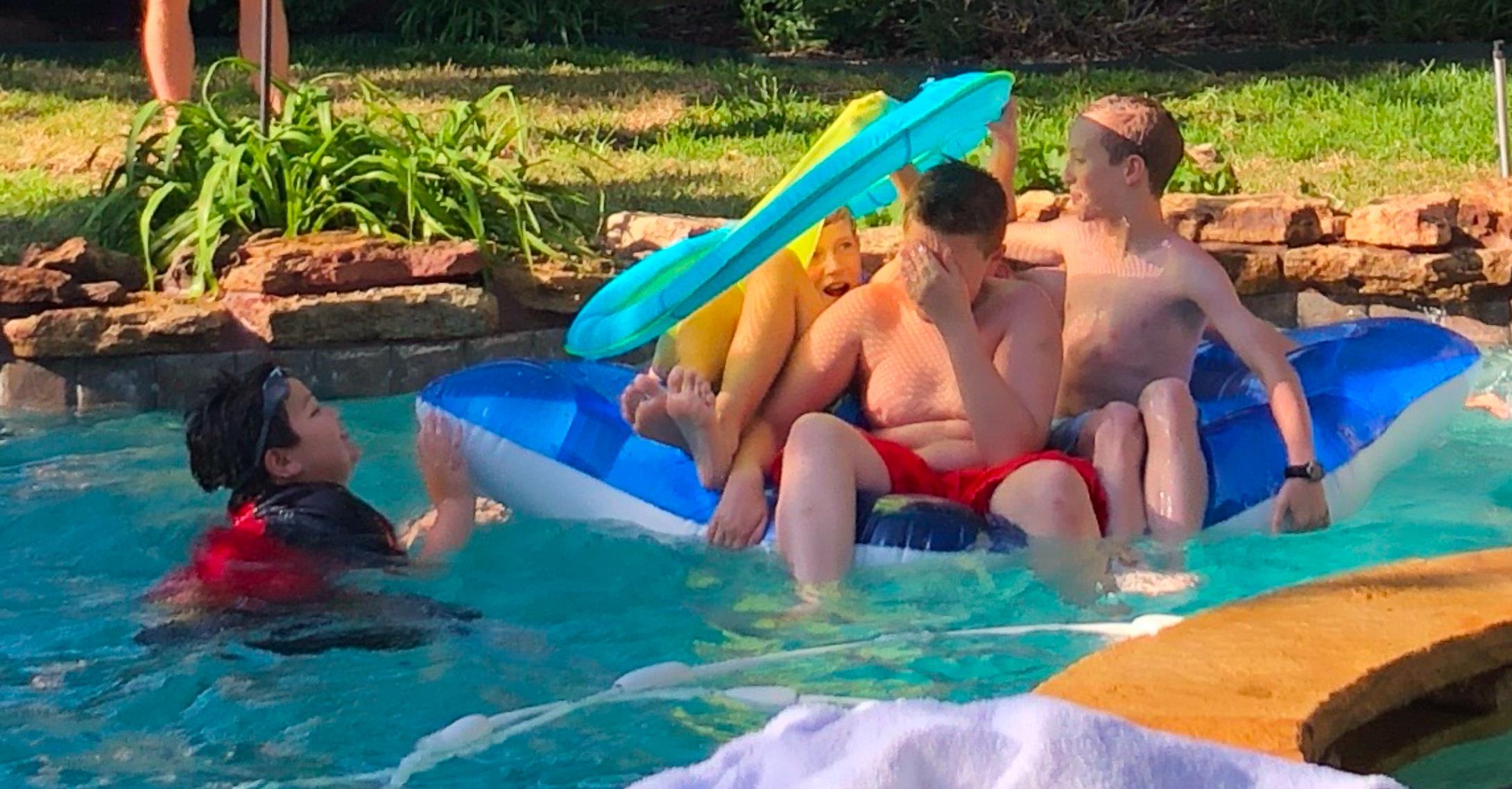 Friends relax and have fun in a backyard swimming pool during a bright summer afternoon.
