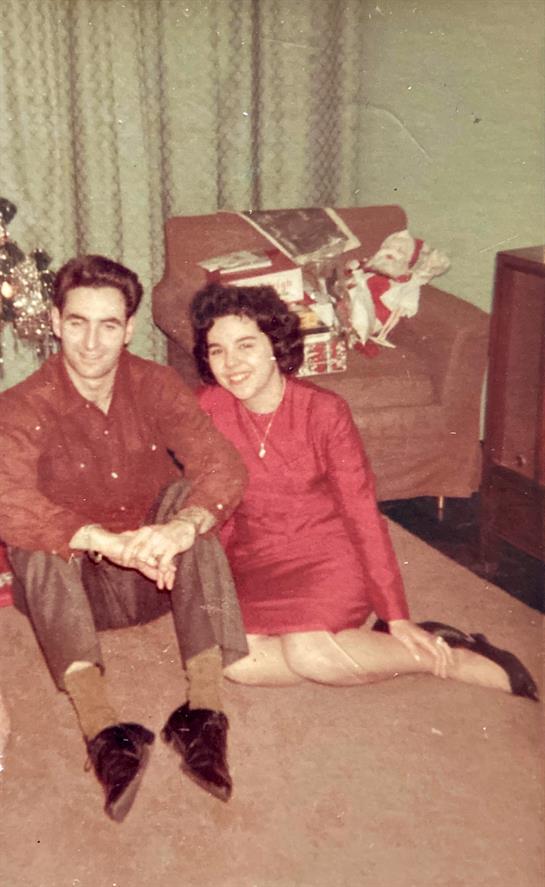 A stylish couple enjoys time together on the floor, surrounded by holiday decorations and presents.