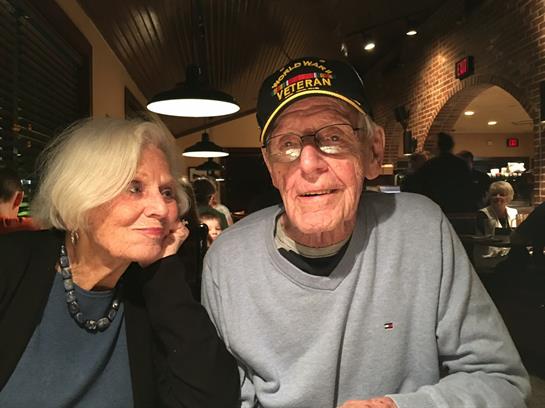An elderly man and woman share conversation and laughter at a warm, inviting restaurant table.