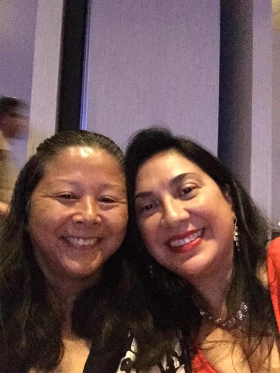 Two women smile and take a selfie while attending a lively social event with friends.