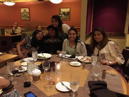 A group of six friends laughs and shares a meal at a restaurant, celebrating together.