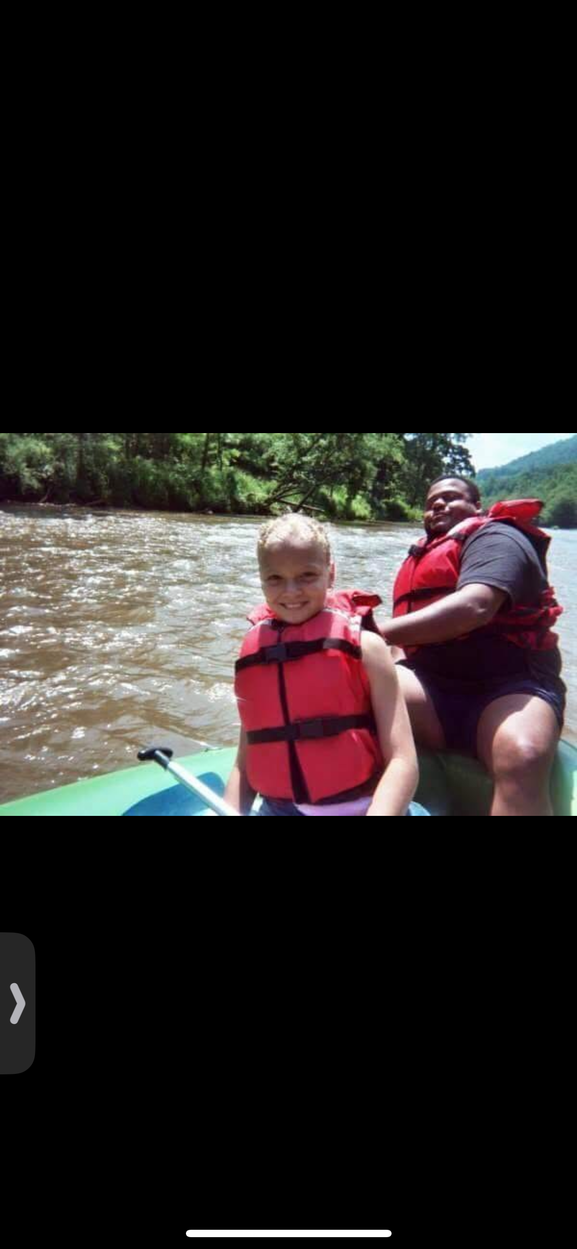 Two friends in bright life jackets enjoy a sunny river trip amid lush greenery.