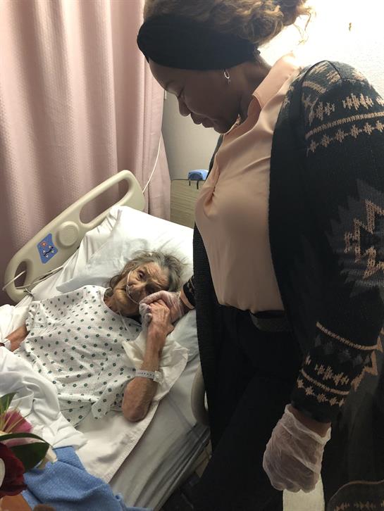 A caregiver holds the hand of an elderly patient, sharing a heartfelt moment in a hospital bed.