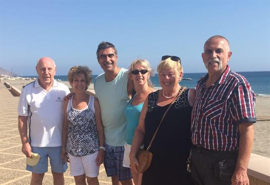 Group of friends stands together, smiling against a beautiful beach backdrop on a sunny day.