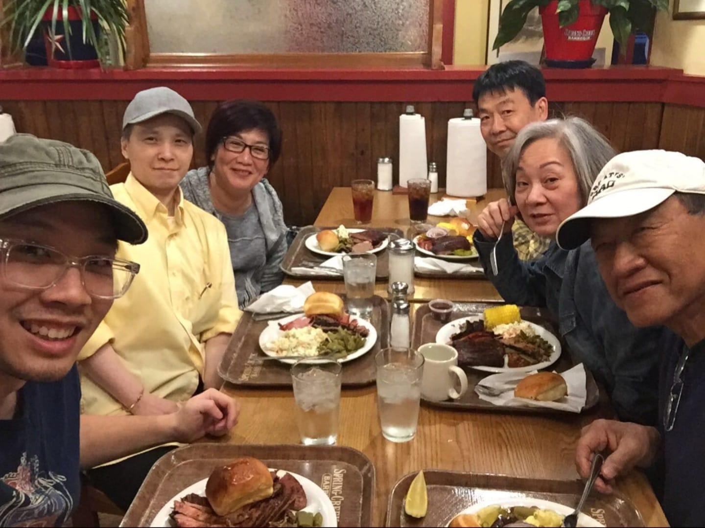Group of six people sharing a meal with plates full of food and drinks at a warm restaurant.