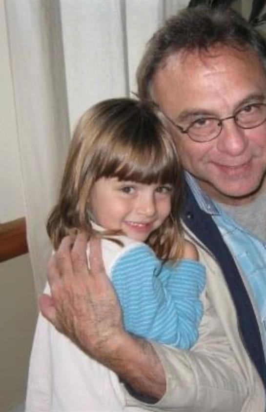 A man embraces a little girl, both smiling happily while enjoying the warmth of companionship.