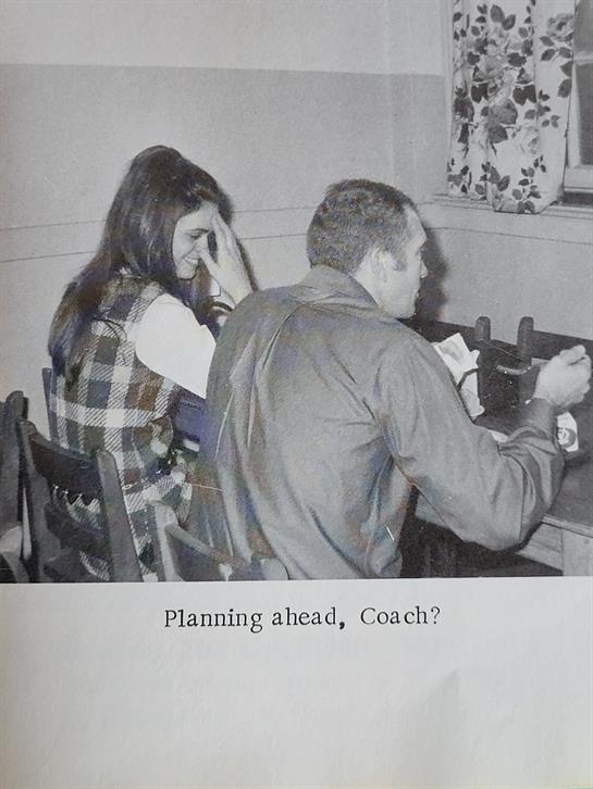 Two people converse at a table, with one appearing thoughtful and the other focused.