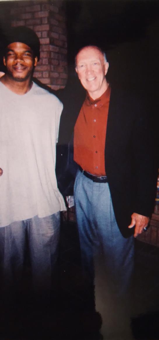 Two men stand together, laughing and enjoying each other's company at a lively event.