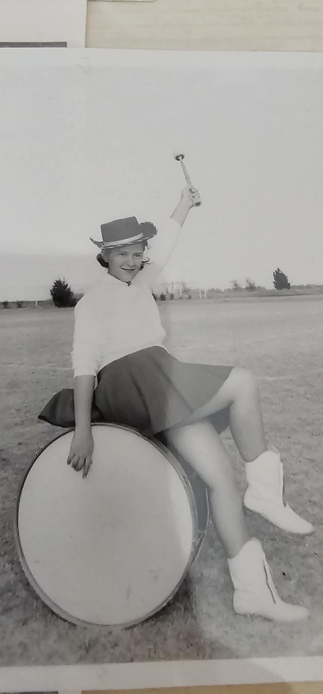 A joyful performer sits on a large drum, raising a baton aloft, celebrating the moment.