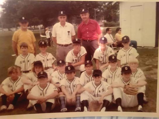 A youth baseball team poses for a group photo at a sunny local park on a summer day.