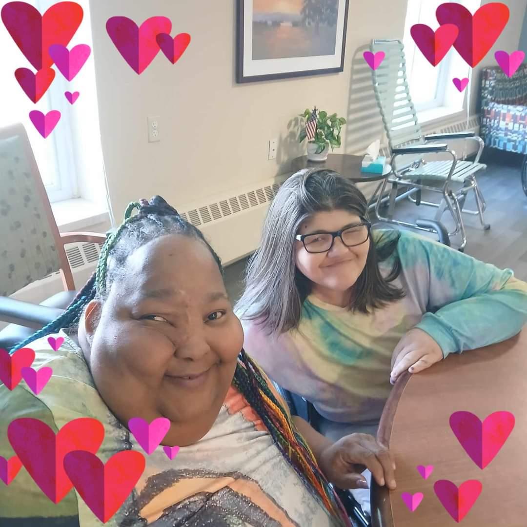 Two women share a joyful moment in a welcoming indoor space decorated with hearts.