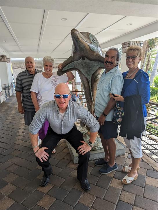 Friends gather around a dolphin sculpture, enjoying a lively moment at a coastal resort.