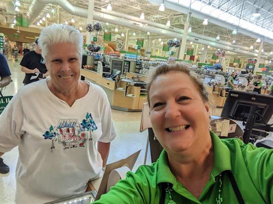 Two women smile warmly while engaging in conversation at a retail checkout area.