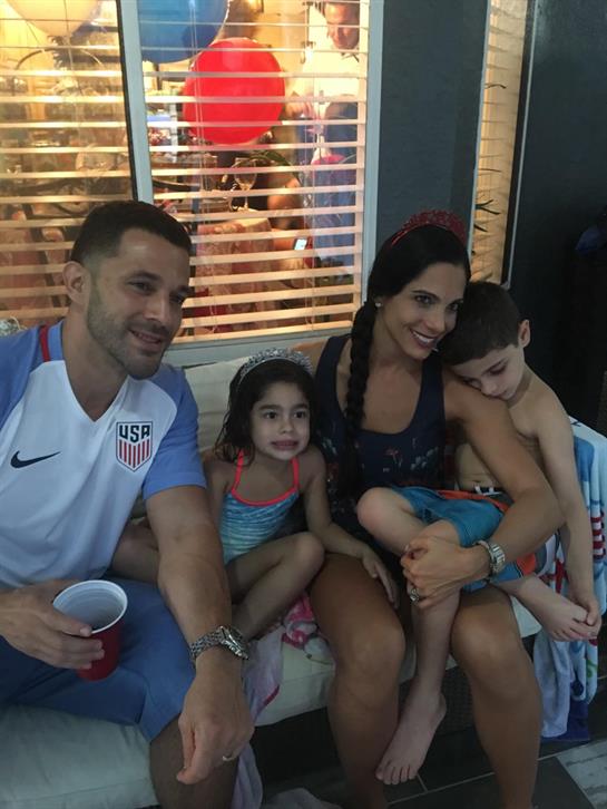 A joyful family relaxes on a couch, celebrating summer while watching their children play.