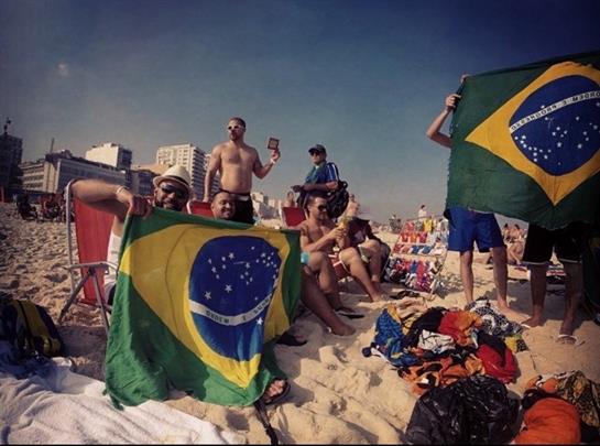 Group of friends enjoy a beach day, showcasing Brazilian flags and celebrating in the sun.