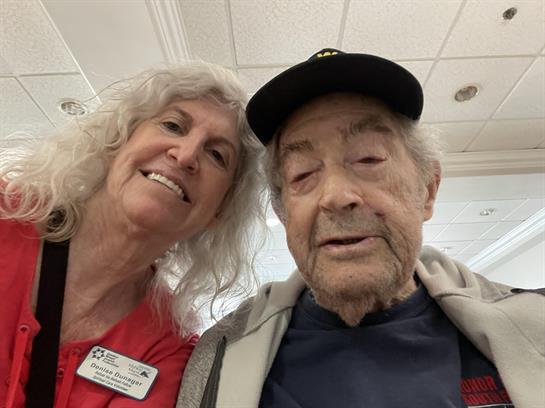 Caregiver and elderly man are smiling together in a cheerful setting at a community center.