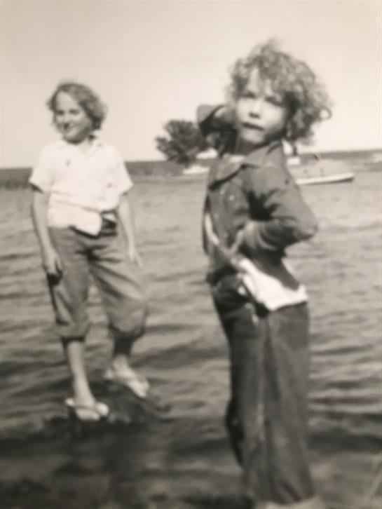 Two children enjoy splashing in the shallow water beside a calm lake under a clear sky.