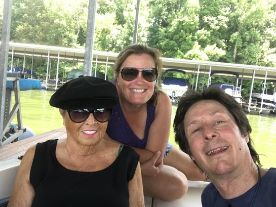 Three family members relax and smile while enjoying a boat ride on a sunny day by the lake.