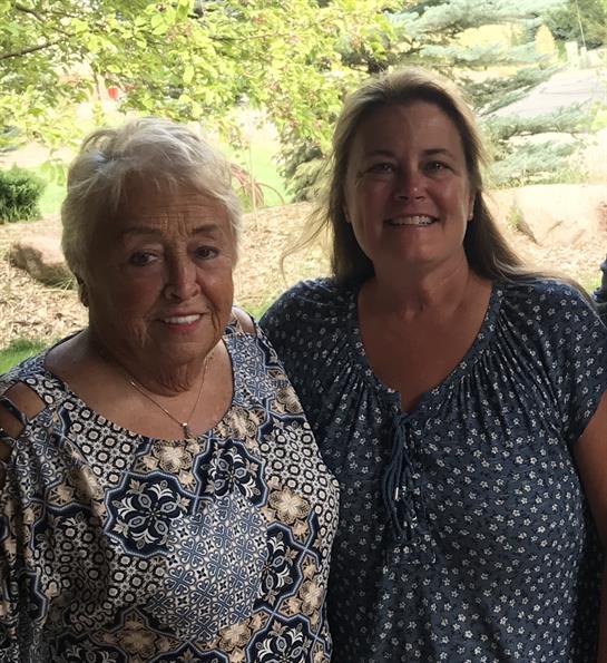 Two women enjoy each other's company in a sunny green space with trees in the background.