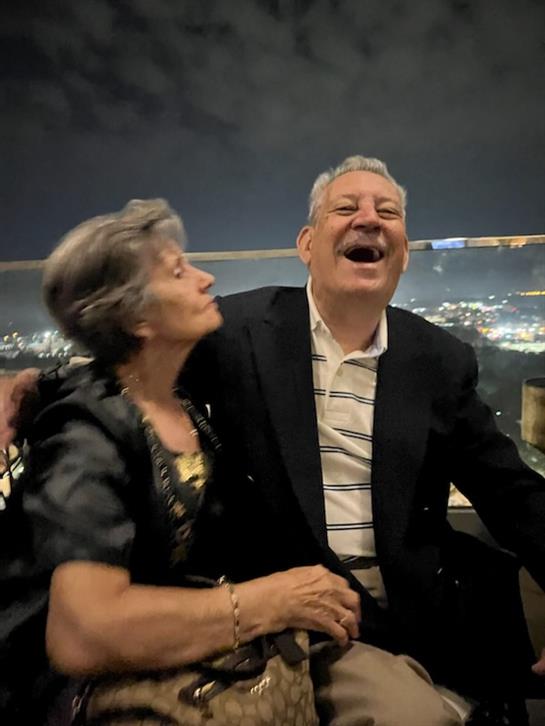 A cheerful elderly couple shares a light-hearted moment while overlooking a city at night.
