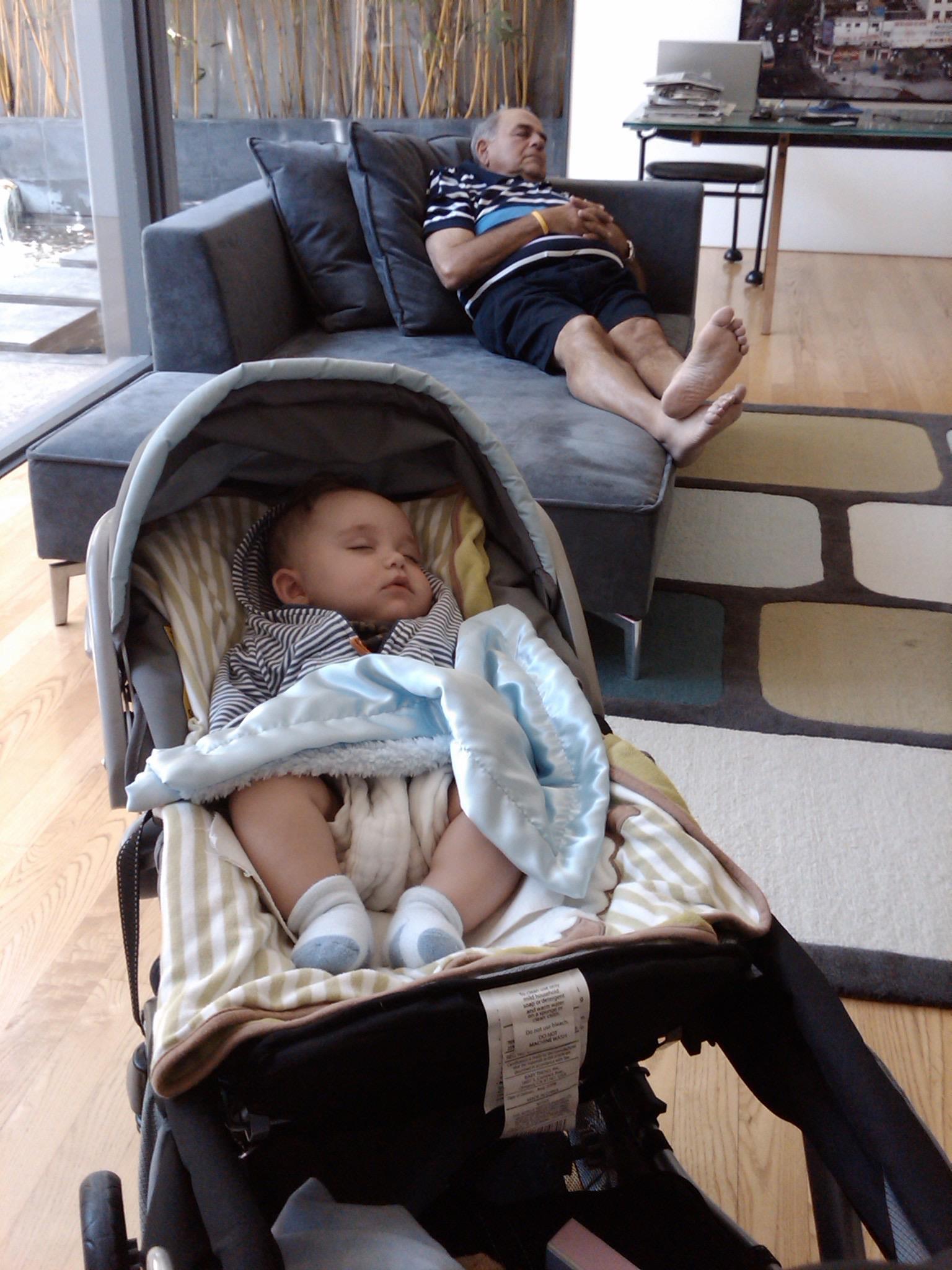 A baby is asleep in a stroller while an older child lounges comfortably on a nearby sofa.