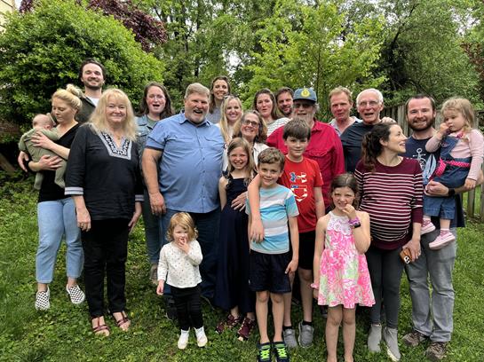 Numerous family members gather in a green garden, enjoying sunlight and each other's company.